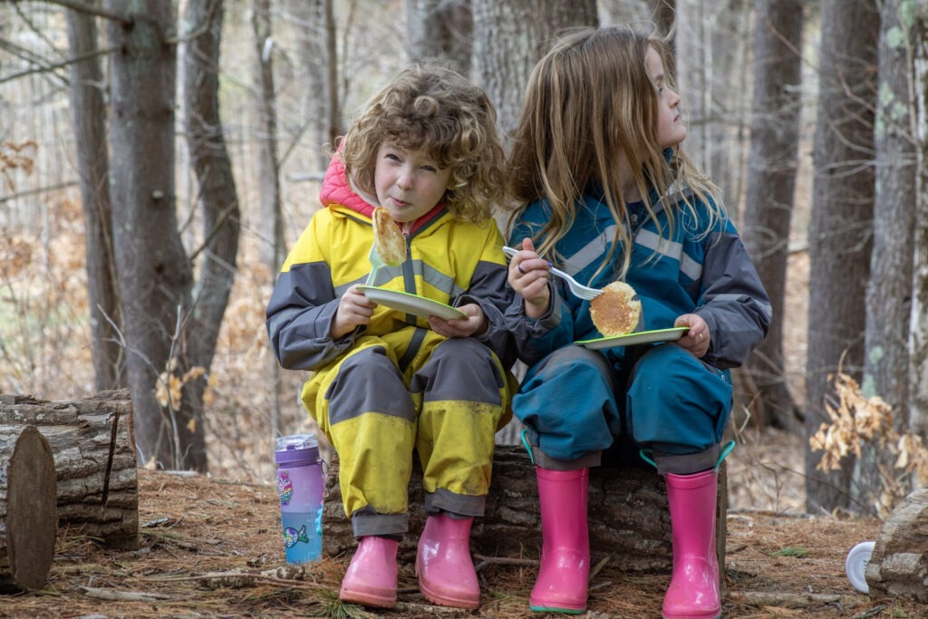 Two students sitting on a rock wearing raincoats and rubber boots in WCS outdoor ed forest